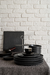 白砖墙背景的桌子上堆放着黑色陶瓷盘子和餐具