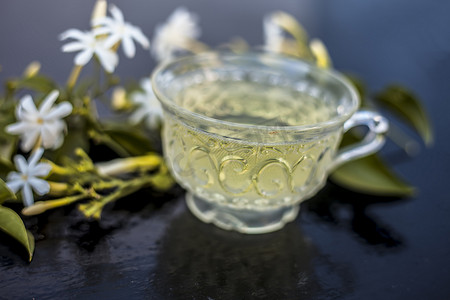 三叶草花摄影照片_印度茉莉花茶或 Juhi 或 Jasminum Auriculatum 茶的特写，在玻璃杯的木质表面上，上面有生花。