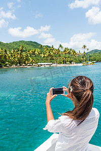 热门句子摄影照片_岸上游览船游览的妇女用手机拍摄圣卢西亚热门旅游景点的照片。