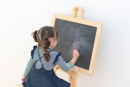 快乐的亚洲女孩在黑板上用粉笔画卡通，供在家学习