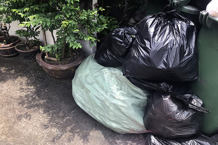 垃圾袋塑料袋摄影照片_垃圾堆成堆，人行道社区村有许多垃圾塑料袋黑色垃圾，垃圾塑料垃圾造成的污染，塑料垃圾袋箱，垃圾堆，垃圾堆
