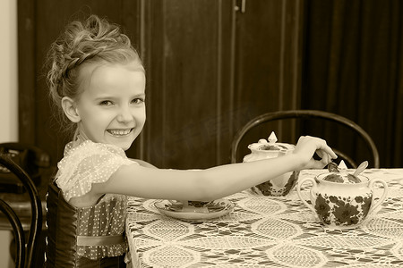 可爱的小女孩在旧桌旁喝茶。