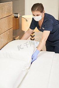 酒店女服务员摄影照片_戴防护手套的女服务员在卧室铺床