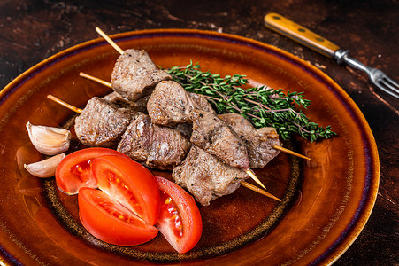 木串烧烤羊肉，质朴的盘子里放着蔬菜。