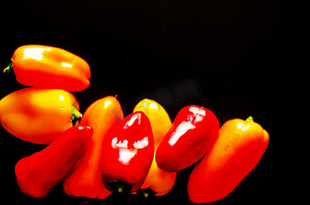 黄黑色背景摄影照片_黑色背景中的红黄辣椒，健康美味的素食产品