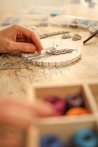 轴流式压缩机摄影照片_特写镜头中，女手在木桌上用 kumihimo 制作流苏手链，配有工具、线轴、天然宝石和彩色珠子