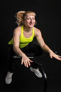 黑色背景健身蹦床上的女孩身穿黄色 T 恤能量女性，有趣的女性跳跃运动，可爱的年轻肌肉教练享受