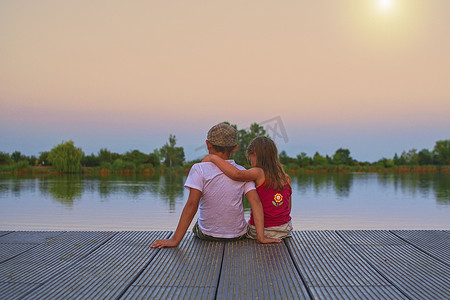 戴平顶帽的男孩和小女孩坐在码头上。