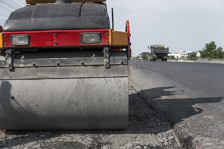 橙色振动压路机站在沥青路附近的地面上进行道路施工和修复沥青路面工程与蓝天。