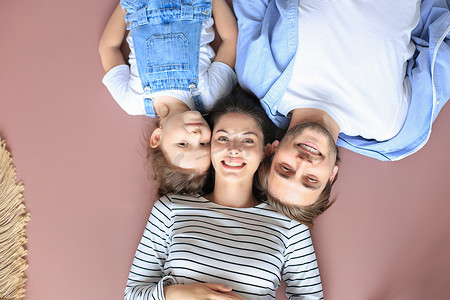 微笑的年轻父母与学龄前儿童的小女儿躺在家里温暖的地板上放松的顶视图肖像，幸福的家庭与小孩休息在家里玩得开心。