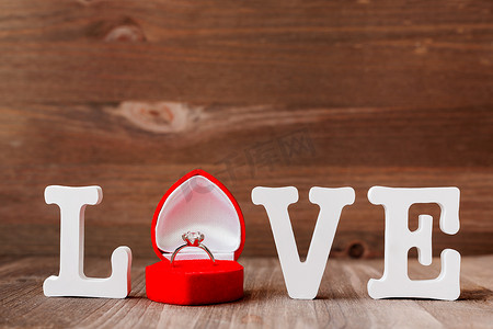 木制背景红色礼品盒中的“爱”字和钻石订婚戒指。