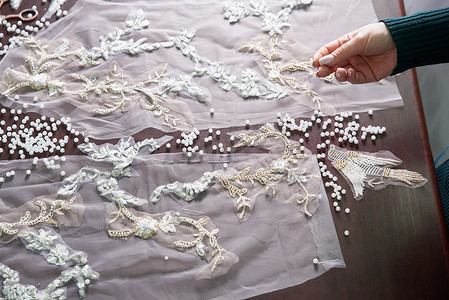 在工作室里用珠子和蕾丝缝制婚纱的女裁缝女手特写