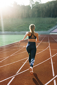 运动员女子在晨光中在赛道上快速奔跑、刻苦训练、为比赛或马拉松比赛做准备的后视图。