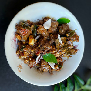 美味的印度风味辣椒羊肉，精美地放在白碗里，碗里放着洋葱和咖喱叶，对骨头有好处