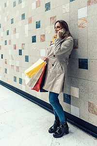 成年女性拿着彩色购物袋打电话。