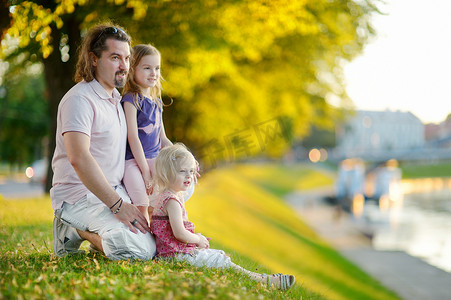 年轻的父亲和他的女儿们坐在河边