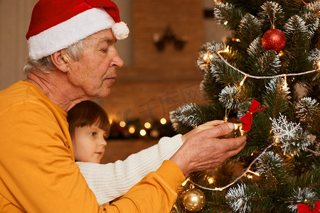 祖父和孙女在装饰杉树的节日房间里，小女孩与成熟的男人一起庆祝除夕夜，圣诞快乐。