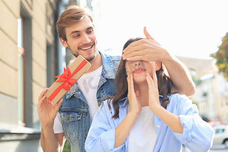 站在城市街道上，穿着夏装的一对兴奋的夫妇微笑着拿着礼物盒在一起。