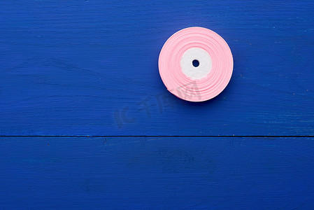 蓝色木质背景上带粉色丝带的圆形线轴