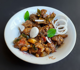 鸡块摄影照片_美味的印度风味辣椒羊肉，精美地放在白碗里，碗里放着洋葱和咖喱叶，对骨头有好处