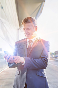 在机场使用带镜头光晕的智能手机的成熟商人肖像