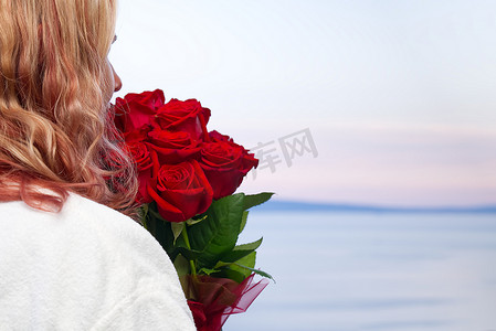 从酒店的海边阳台望去，身穿白袍、手捧红玫瑰的快乐女人