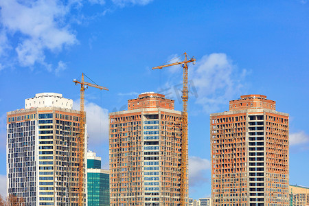 基础建设详情页摄影照片_现代住宅摩天大楼的建设，有玻璃幕墙和塔式起重机在蓝天的衬托下。