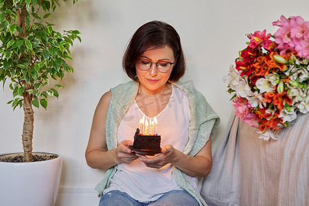 生日、庆典、周年纪念日，45 岁的女人带着点着蜡烛的小蛋糕