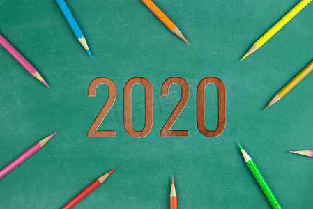绿色黑板上的木文字 2020 和彩色铅笔
