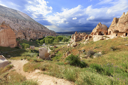 一条土路蜿蜒在圆锥形的岩石山峰和古老的洞穴之间，以卡帕多西亚山谷的山景为背景