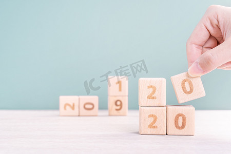 摘要 2020 年和 2019 年新年倒计时设计理念 — 女性在木桌和绿色背景上拿着木块立方体，特写，复制空间。