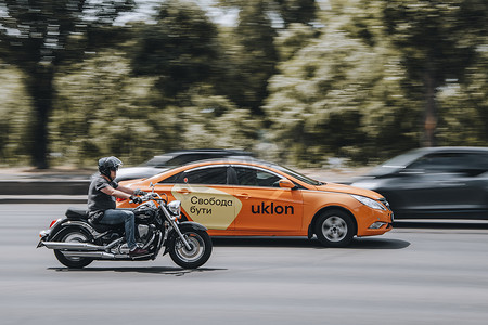 乌克兰，基辅 - 2021 年 6 月 27 日：铃木入侵者摩托车与现代索纳塔 Uklon 出租车在街上行驶。