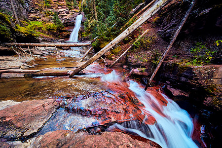 雄伟的瀑布在背景中，层叠的瀑布落在前面的红色岩石上