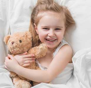 抱着棕色泰迪熊躺在床上的女孩
