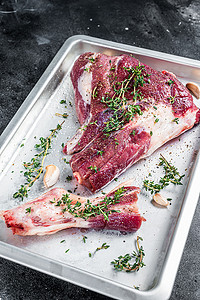 蒸羊腿摄影照片_在烤盘中用百里香、胡椒和橄榄油烹饪生羊肉羊腿。