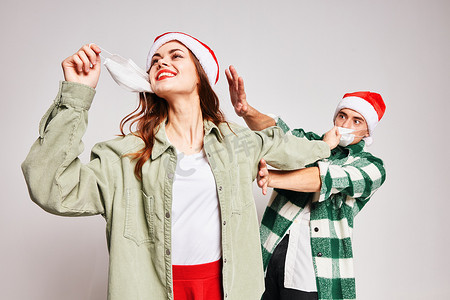 2021年摄影照片_戴圣诞帽的男人和女人一起玩节日医用口罩