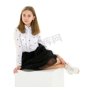 优雅女性摄影照片_坐在白色立方体上的优雅礼服的美丽金发女孩
