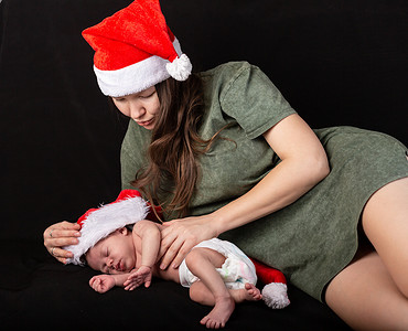 母婴红色摄影照片_身穿圣诞红裙的母婴在深色背景中微笑