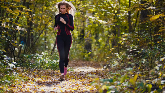 年轻的赛跑者女孩在落叶覆盖的秋天道路上慢跑。