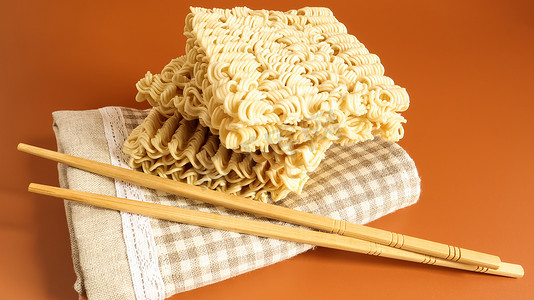 毛巾上的生方便面，黄色背景上有筷子。