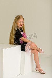 小女孩盘腿坐在白色立方体上。