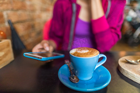 咖啡馆里的女人用手机应用程序喝卡布奇诺咖啡杯。