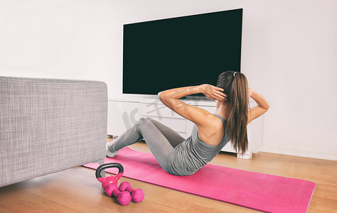 家庭健身女性在家里或公寓的客厅里做力量训练 abs 仰卧起坐体重地板练习观看在线直播锻炼网络视频投射在智能电视上
