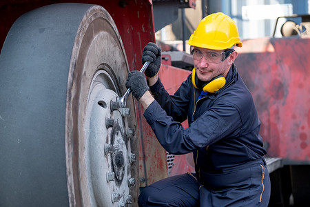 集装箱技术人员或工人使用扳手来解决卡车轮胎的问题，并在工作区域工作时查看摄像头。