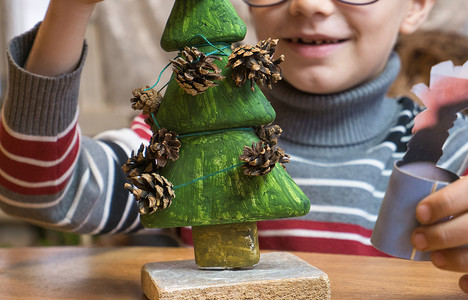 一个小男孩用松果装饰一棵手工制作的圣诞树，同时玩耍。