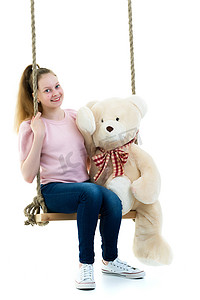 一个小女孩正抱着一只泰迪熊荡秋千。