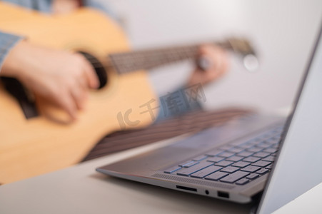 年轻的白人女性，留着金色短发，弹着吉他，在笔记本电脑上观看培训视频。