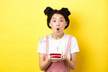 生日快乐的亚洲女孩，妆容鲜艳，在蛋糕上吹蜡烛，许愿，站在黄色背景上