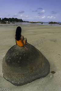 穿着橙色裙子坐在大石头上的女人