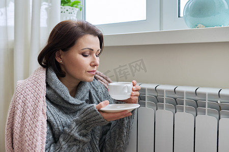 散热器摄影照片_冬季，妇女在家庭暖气散热器附近取暖